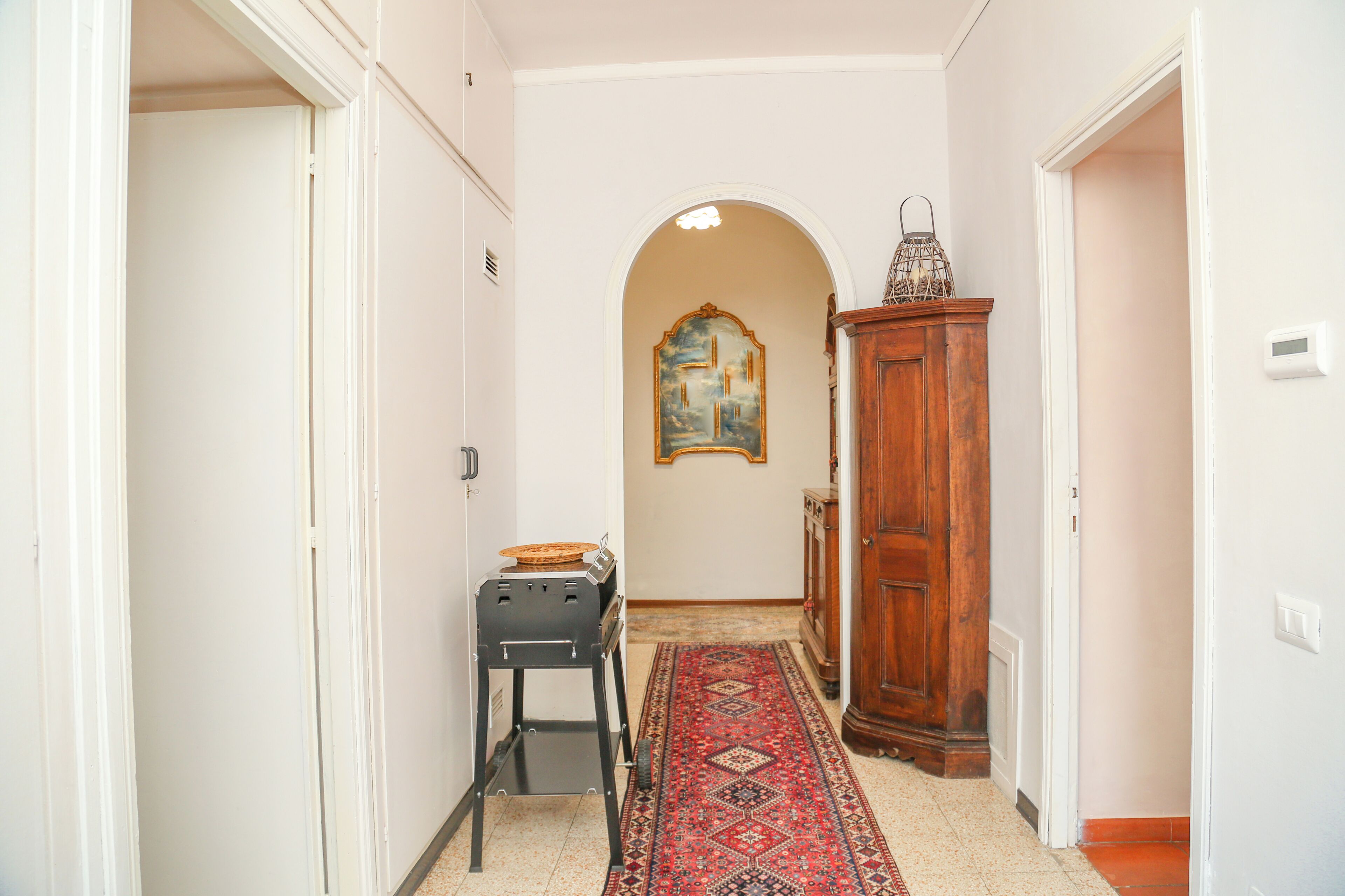 A hallway with a patterned rug, a wooden cabinet, and a painting on the wall.