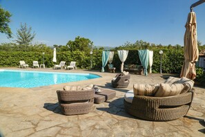 Zona junto a la piscina con muebles de mimbre, un área de estar cubierta y un cielo azul despejado.