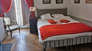 Une chambre à coucher avec un lit, une chaise, une table de chevet et une fenêtre avec des rideaux rouges.