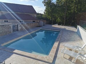 Une piscine rectangulaire bordée de pierres, entourée d’une terrasse dallée de pierres et agrémentée de chaises longues blanches.