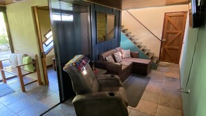 Un área de estar acogedora con un sofá y un sillón, una escalera y un ventanal corredero hacia el exterior.