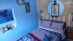 Une chambre avec un mur bleu, une tête de lit en bois, un lit avec une literie à rayures, un luminaire suspendu et un miroir fixé au mur.