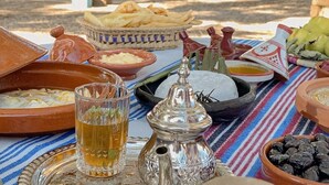 Un assortiment traditionnel de plats marocains, accompagné de pain et de boissons, disposé sur une nappe à rayures.