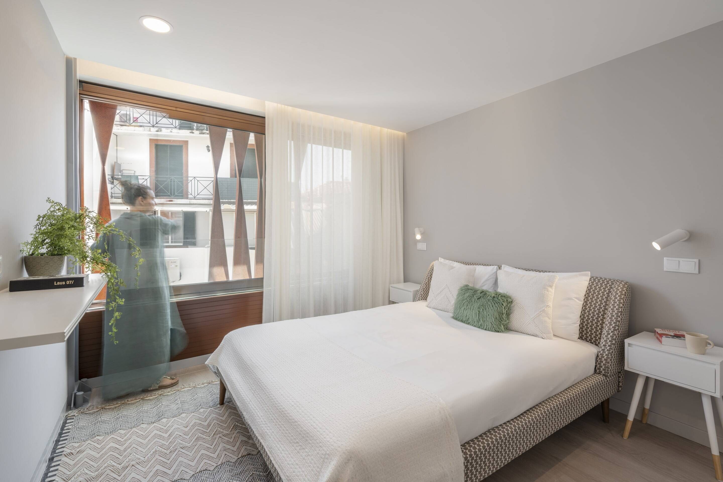 Una camera da letto moderna con un letto grande, un comodino, una lampada da tavolo e una finestra con tende, oltre a un vaso con una pianta.