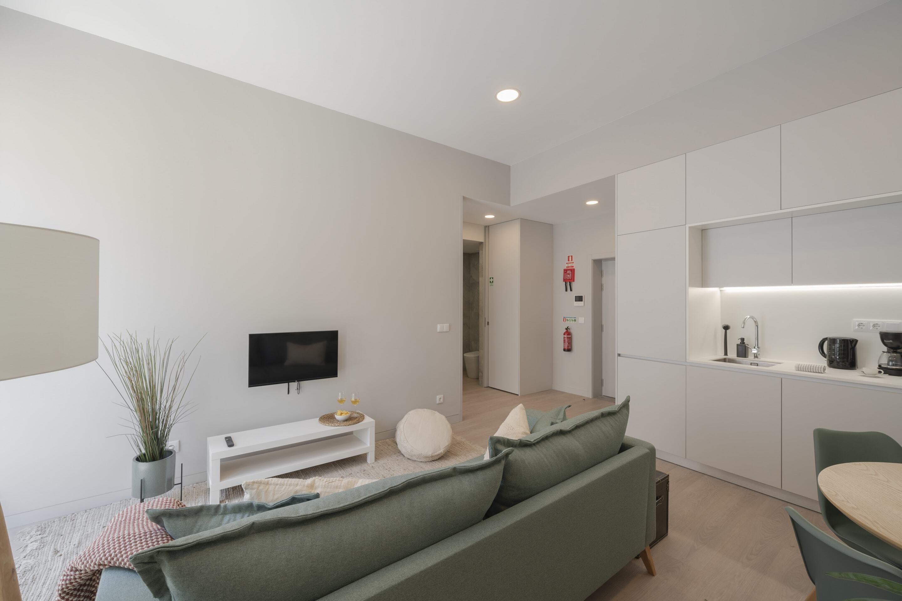 A modern living room with a green sofa, a flat-screen TV, and a small white table.