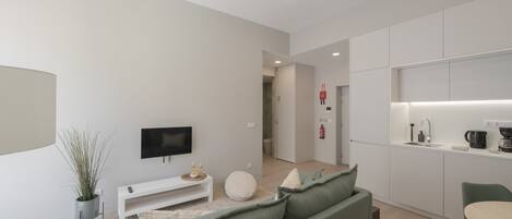A modern living room with a green sofa, a flat-screen TV, and a small white table.