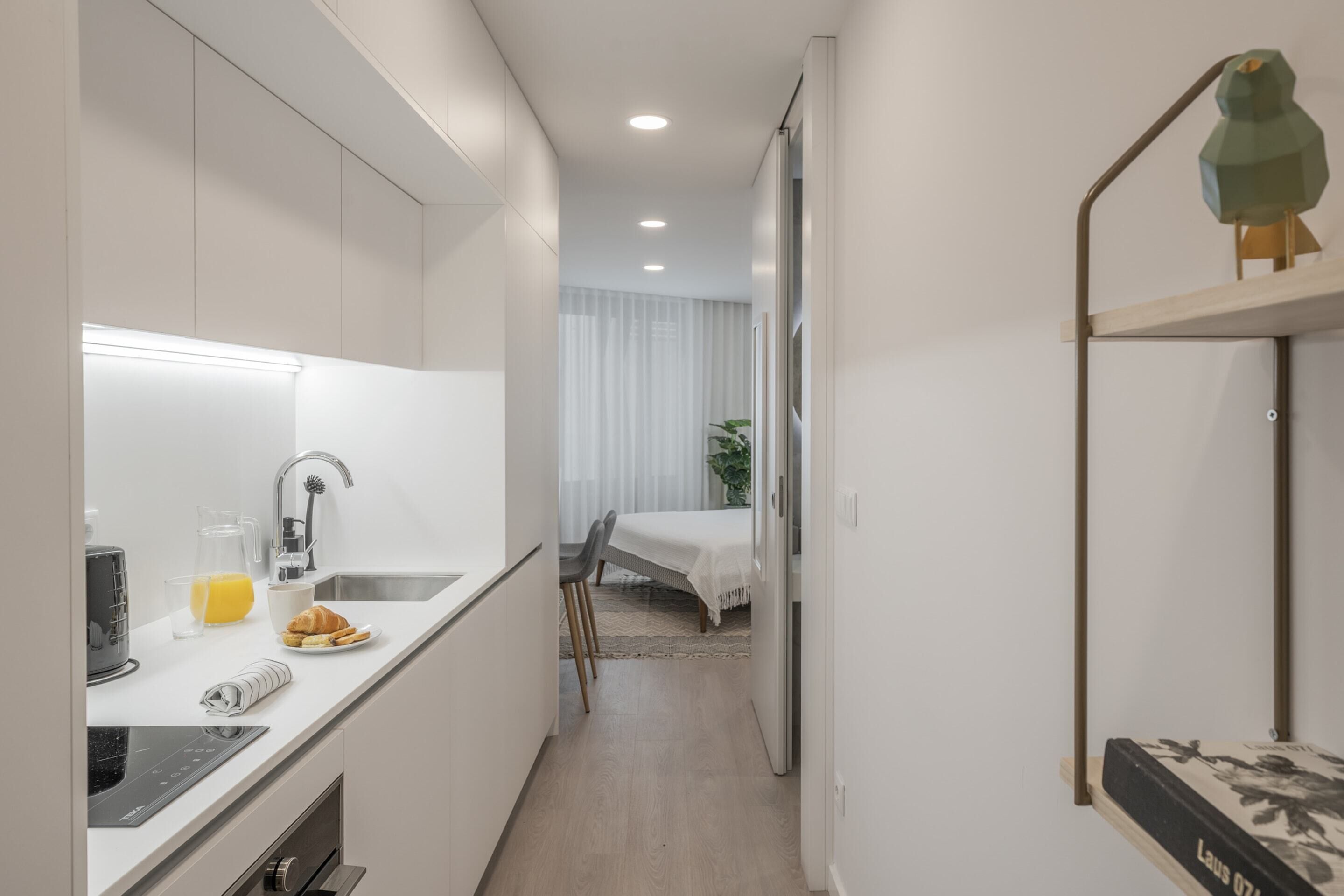 A narrow, modern kitchen with a built-in oven, a sink, and a breakfast bar.
