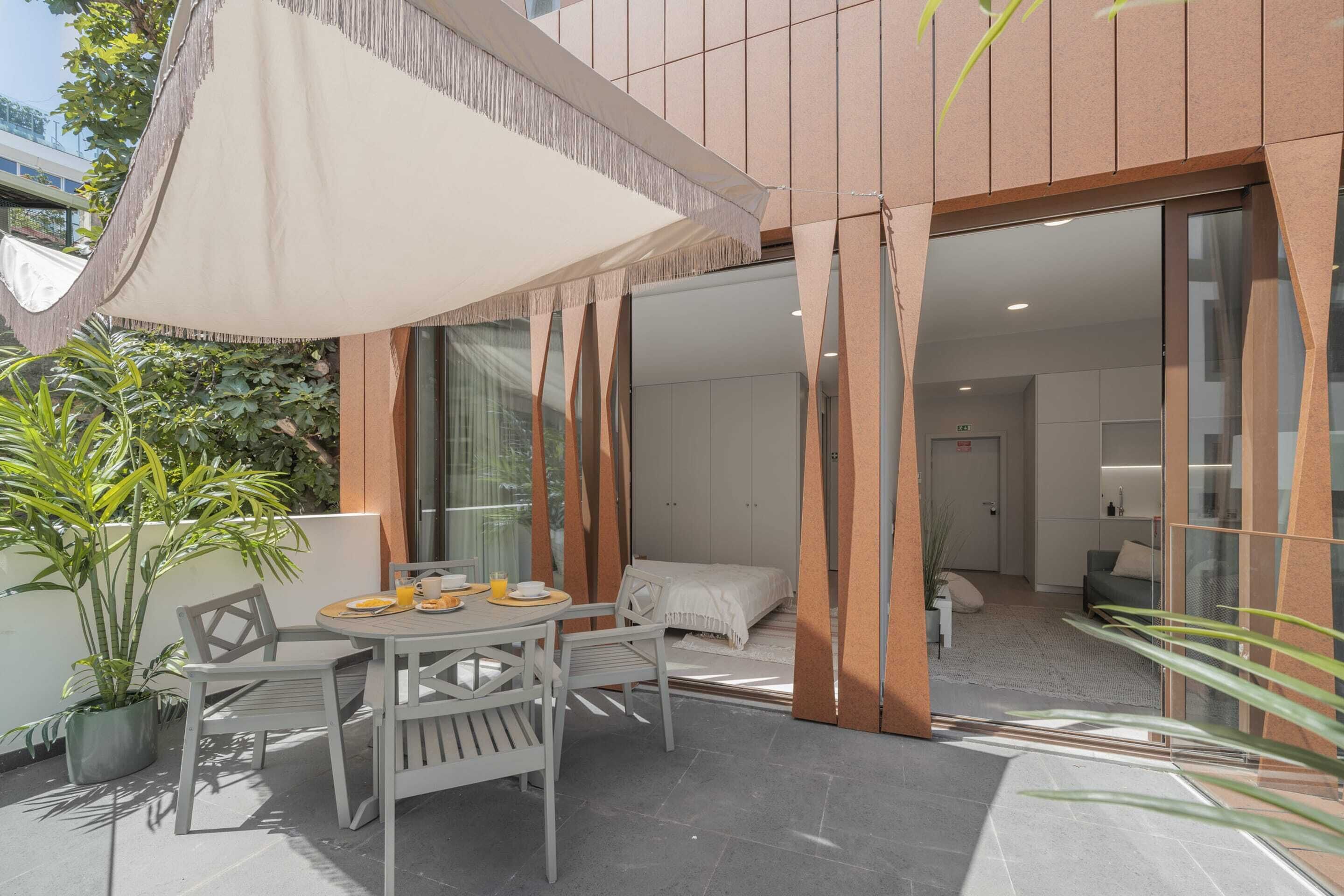 An outdoor patio with a table and chairs, a large umbrella, and potted plants.