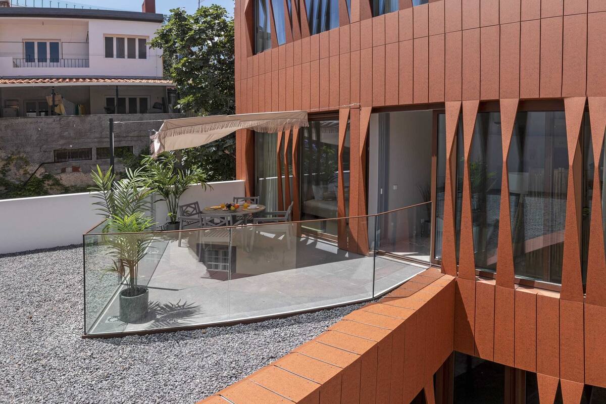 Ein modernes Gebäude mit einem Glasbalkon, Topfpflanzen und Gartenmöbeln.