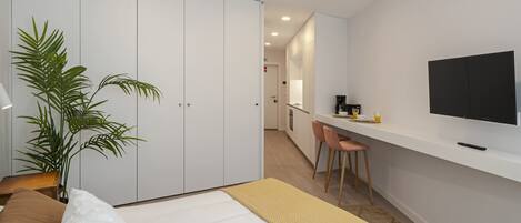 A modern bedroom with a bed, a desk, a chair, a television, and a plant.