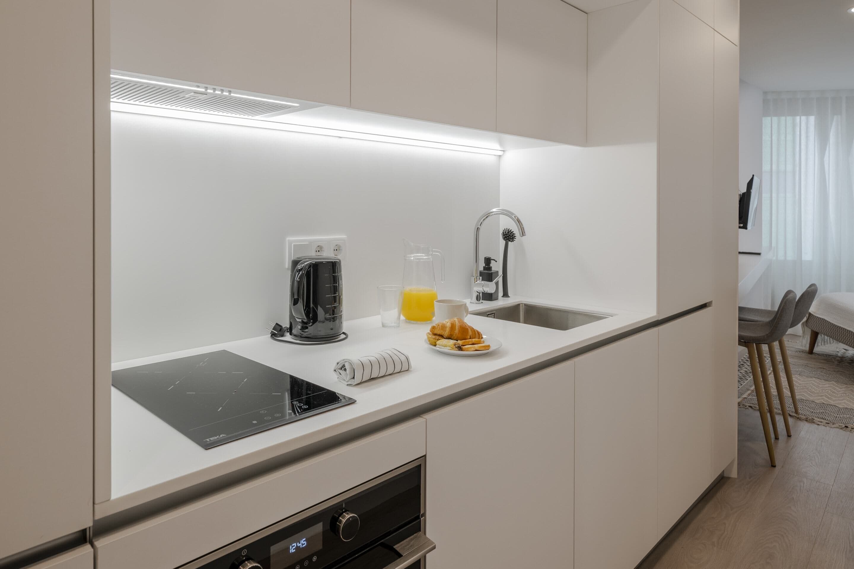 A modern kitchen with a built-in induction cooktop, a coffee maker, a glass pitcher, and a plate of croissants.