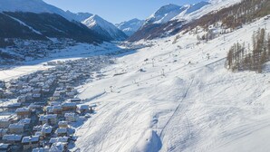 Un pueblo nevado al pie de una montaña con pistas de esquí y una pequeña aldea.