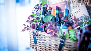 Una cesta de mimbre llena de botellas de vino, incluyendo una botella de vino Lindeman, y un libro titulado 'New Forest'.