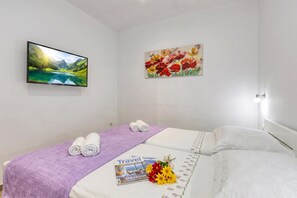 A hotel room with a bed, a television mounted on the wall, and two paintings. - Pool And Garden Apartment Happy Sound (Rijeka)