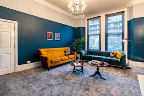 Ein Wohnzimmer mit einem gelben Sofa, einem grünen Sofa, zwei runden Couchtischen und einer Pendelleuchte.