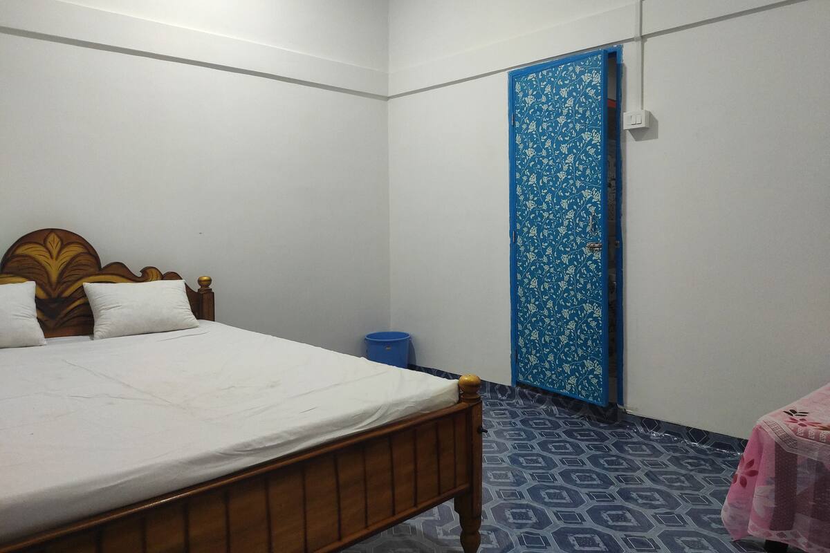 A bedroom with a wooden bed, white walls, a blue door, and patterned floor tiles.