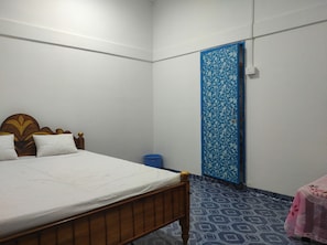 A bedroom with a wooden bed, white walls, a blue door, and patterned floor tiles.