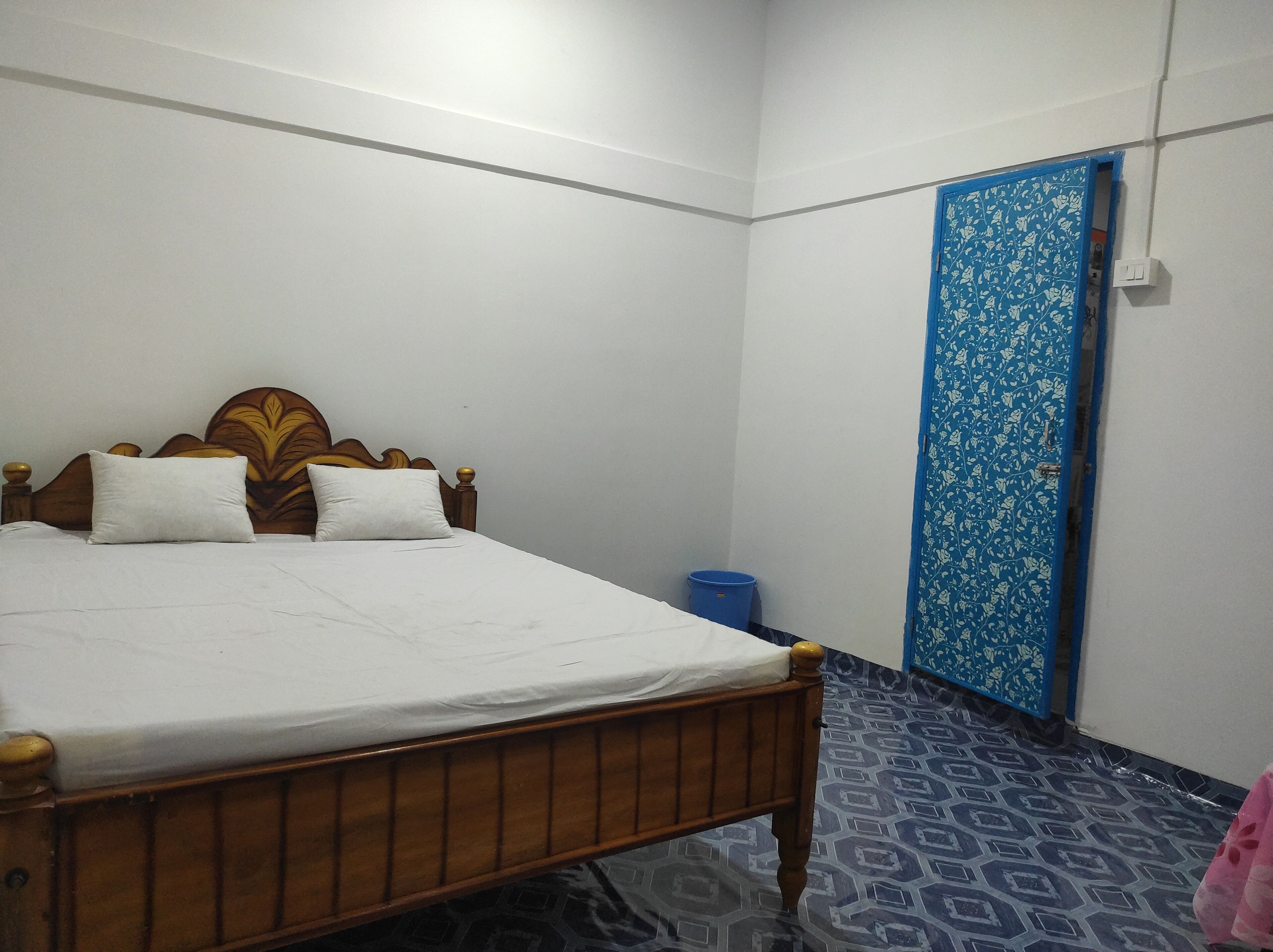 A bedroom with a wooden bed, white bedding, a blue door with floral patterns, and a patterned floor.