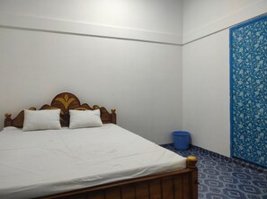 A bedroom with a wooden bed, two pillows, a blue trash bin, and a blue patterned door.