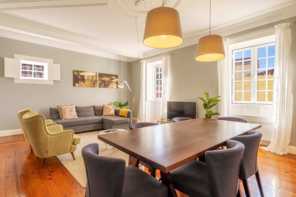 A dining area with a wooden table and six chairs, a sofa, a television, and a window with curtains.