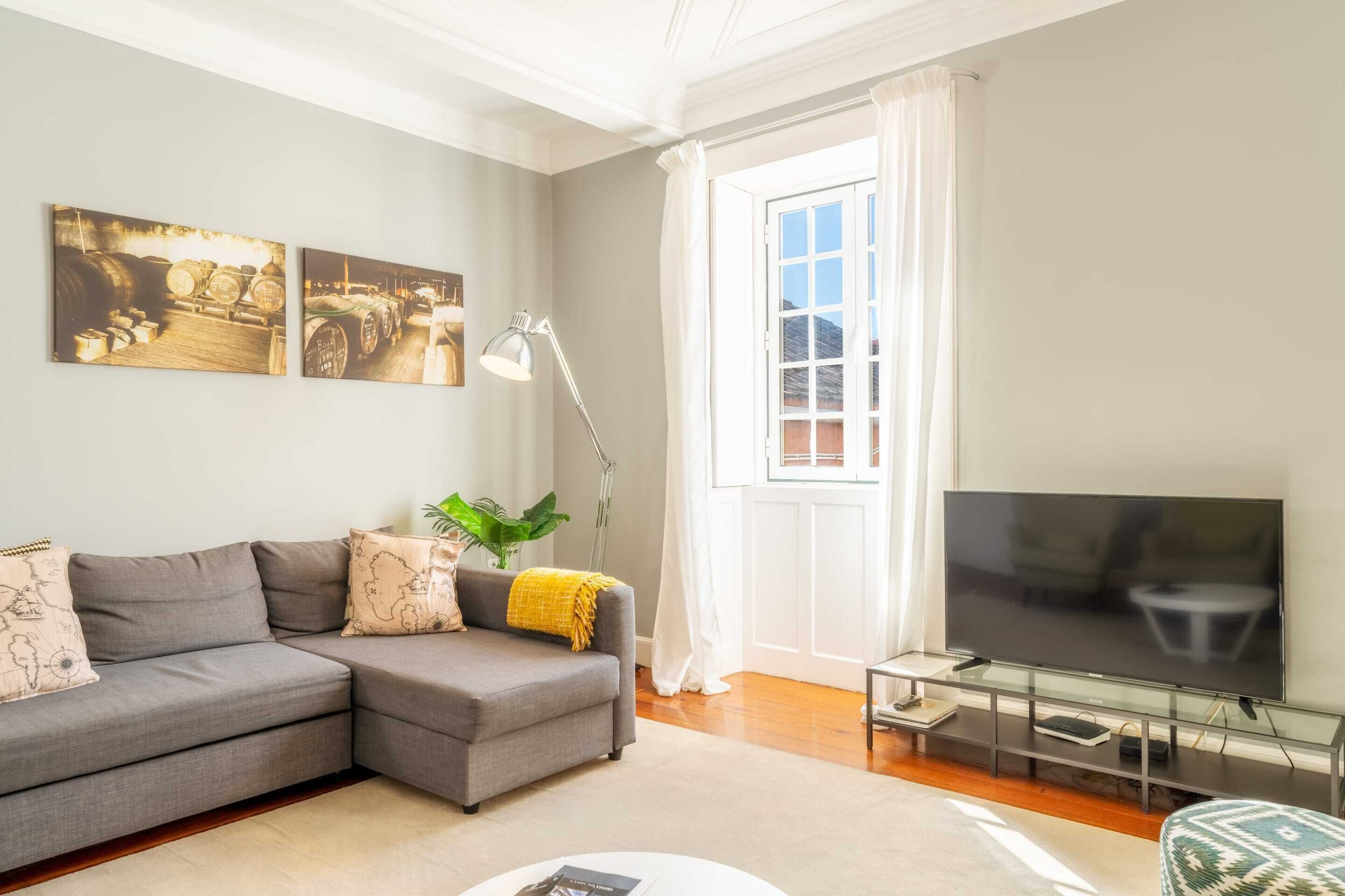 A modern living room with a grey sectional sofa, a flat-screen TV, and artwork on the wall.