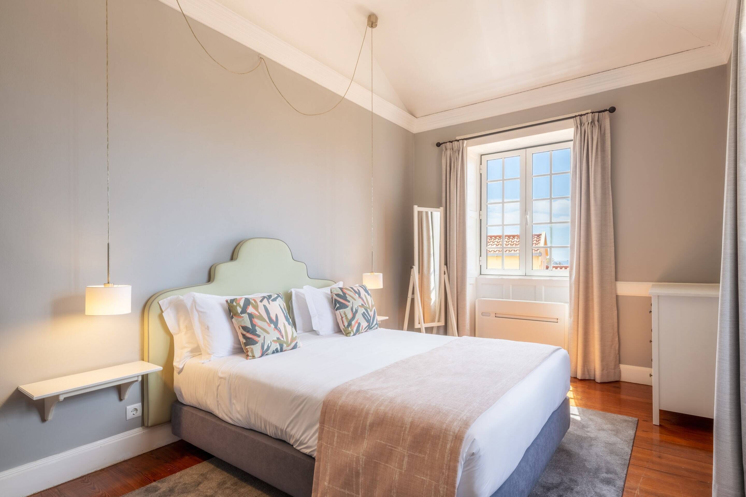 Une chambre à coucher avec un lit, des tables de chevet, une fenêtre avec des rideaux et une vue sur l’extérieur.