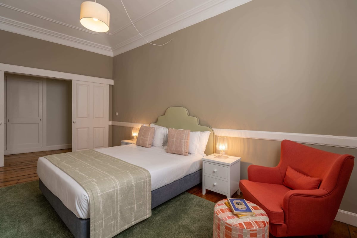 A bedroom with a bed, bedside tables, a nightstand, a chair, and a small table with books.