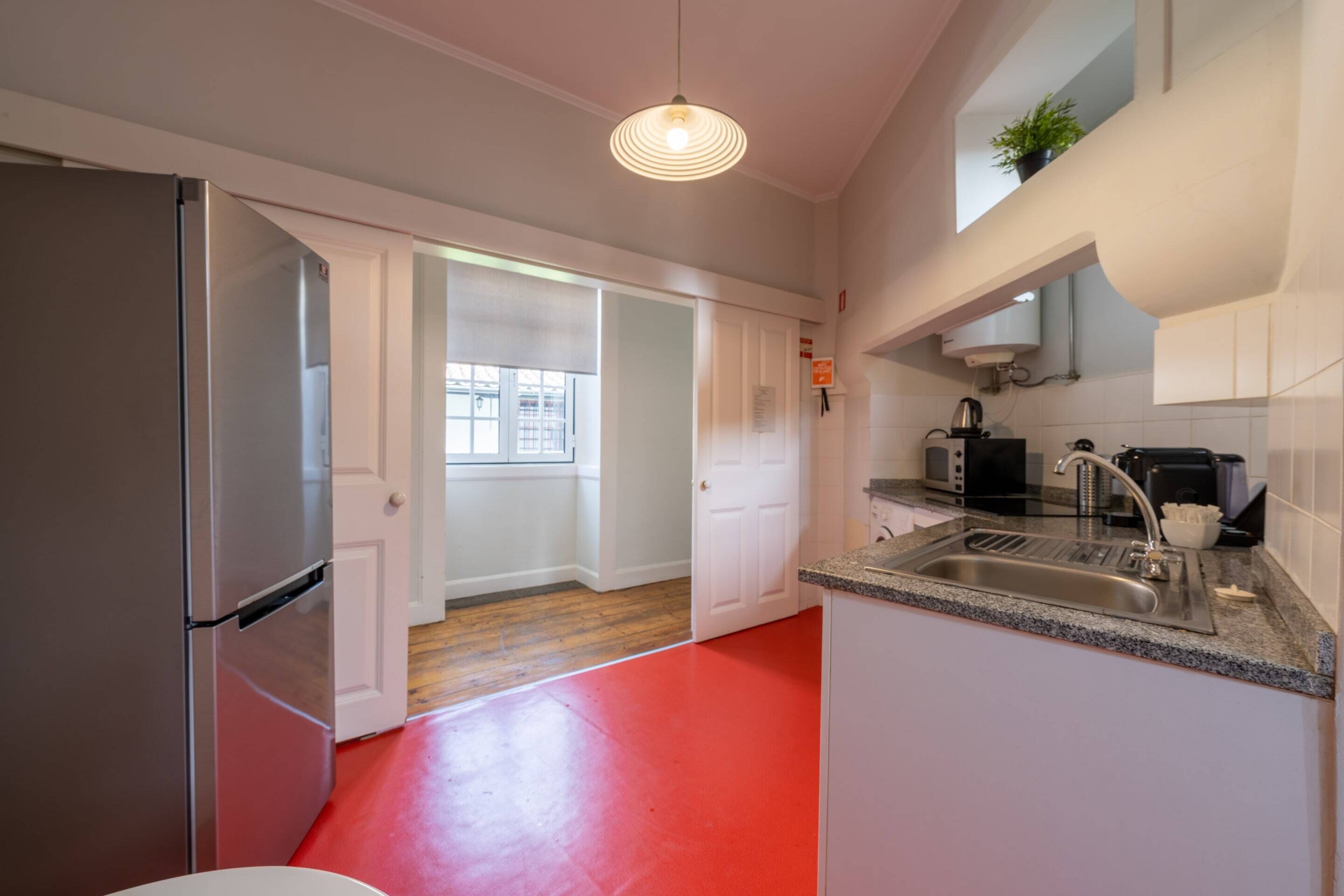 A kitchen with a stainless steel refrigerator, a granite countertop, a sink, and a window with a view of the outside.