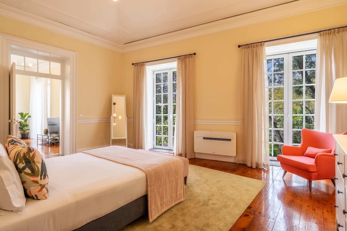 A bedroom with a bed, a chair, a desk, and a window with curtains.