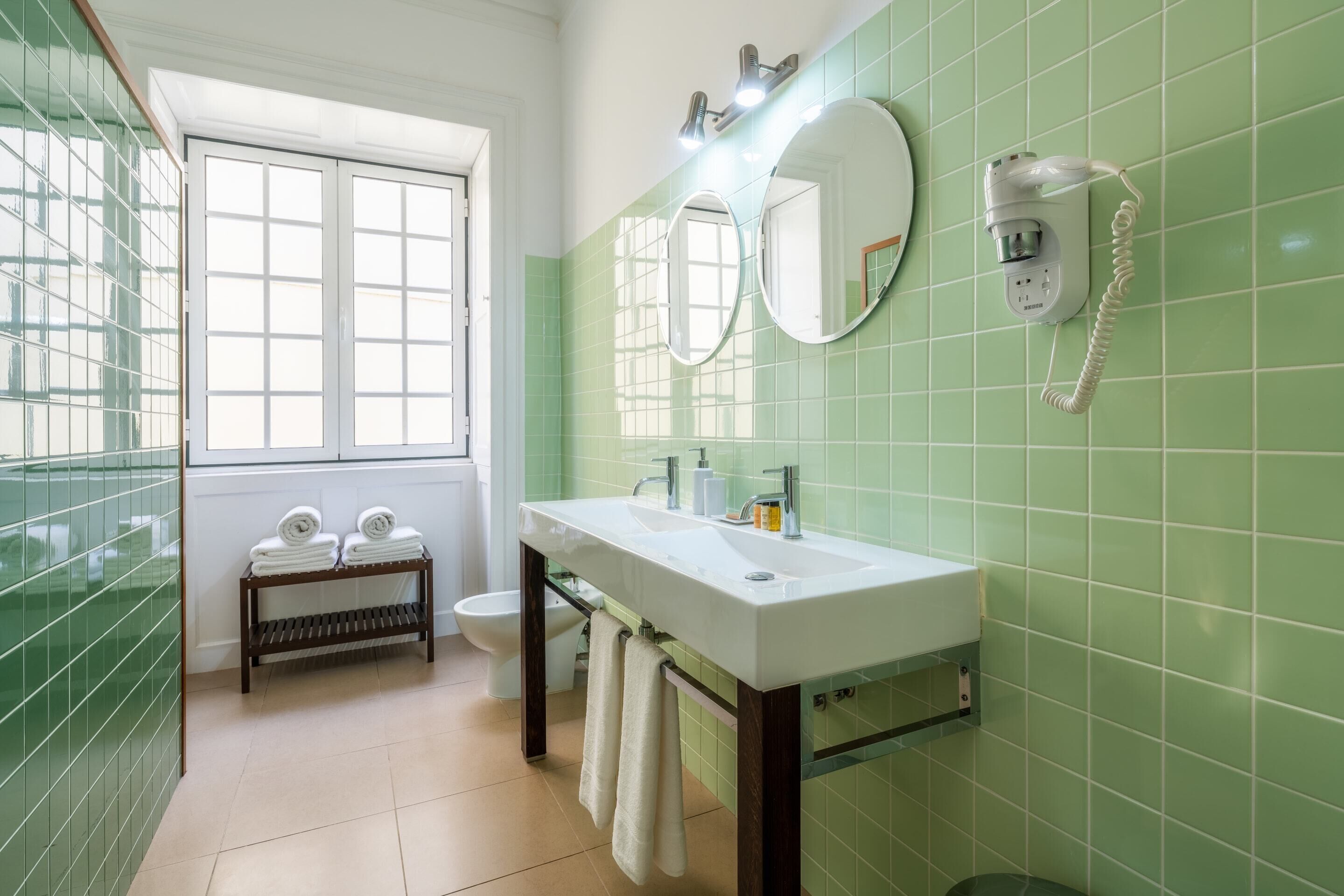 A bathroom with a white sink, two mirrors, a hairdryer, and a toilet.
