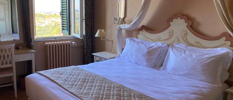 A neatly made bed with a quilted bedspread, a bedside table with a lamp, and a window with shutters.
