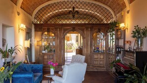 A spacious living area with a grand arched doorway, a blue sofa, a white armchair, a piano, and various plants. - Quattro Gigli Palace (Montopoli in Val d'Arno)