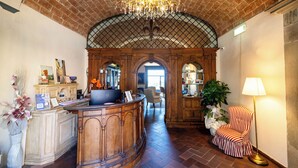 A lobby with a reception desk, a chandelier, a striped armchair, and a large plant. - Quattro Gigli Palace (Montopoli in Val d'Arno)
