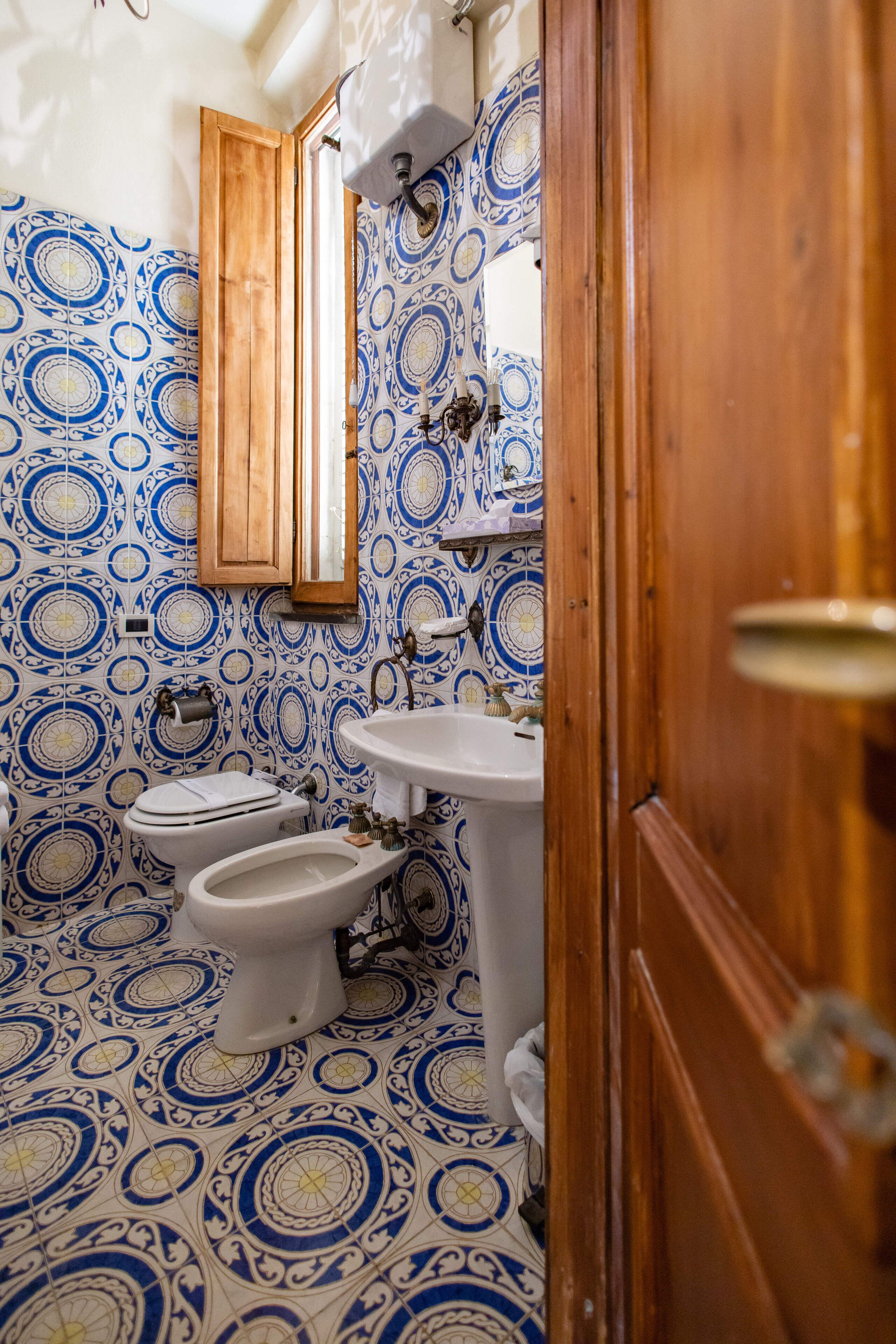 Un baño con piso azul y blanco estampado, una puerta de madera y un lavamanos blanco.