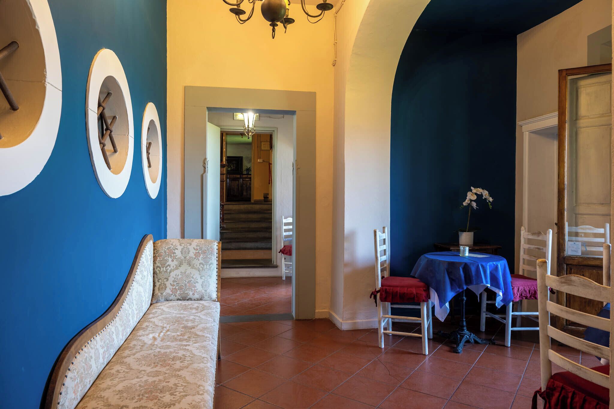 Una habitación con una pared azul, un sofá, una mesa de comedor con sillas y una escalera al fondo.
