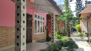 Une cour avec un mur en briques, un bâtiment rose doté d’une fenêtre et des plantes en pot.
