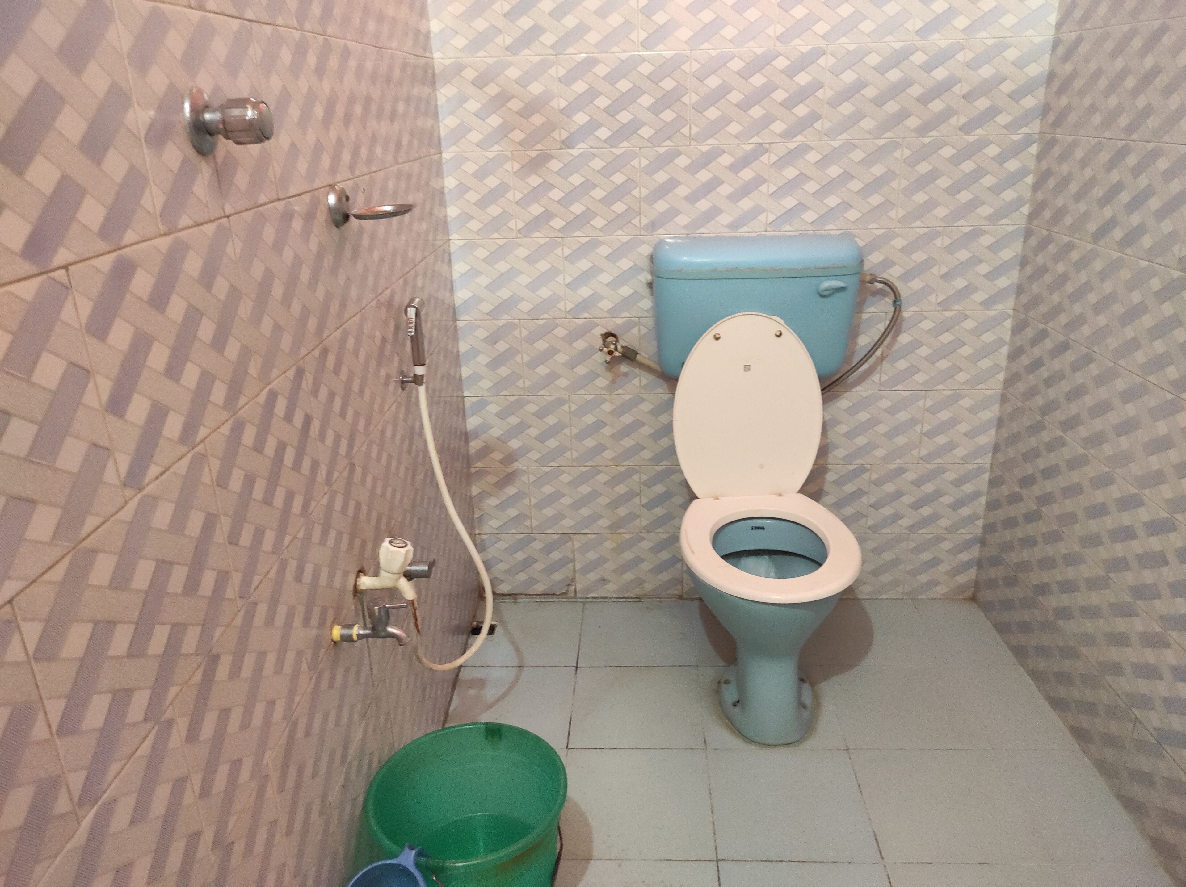 Un baño con inodoro, ducha y un cubo verde en el suelo.