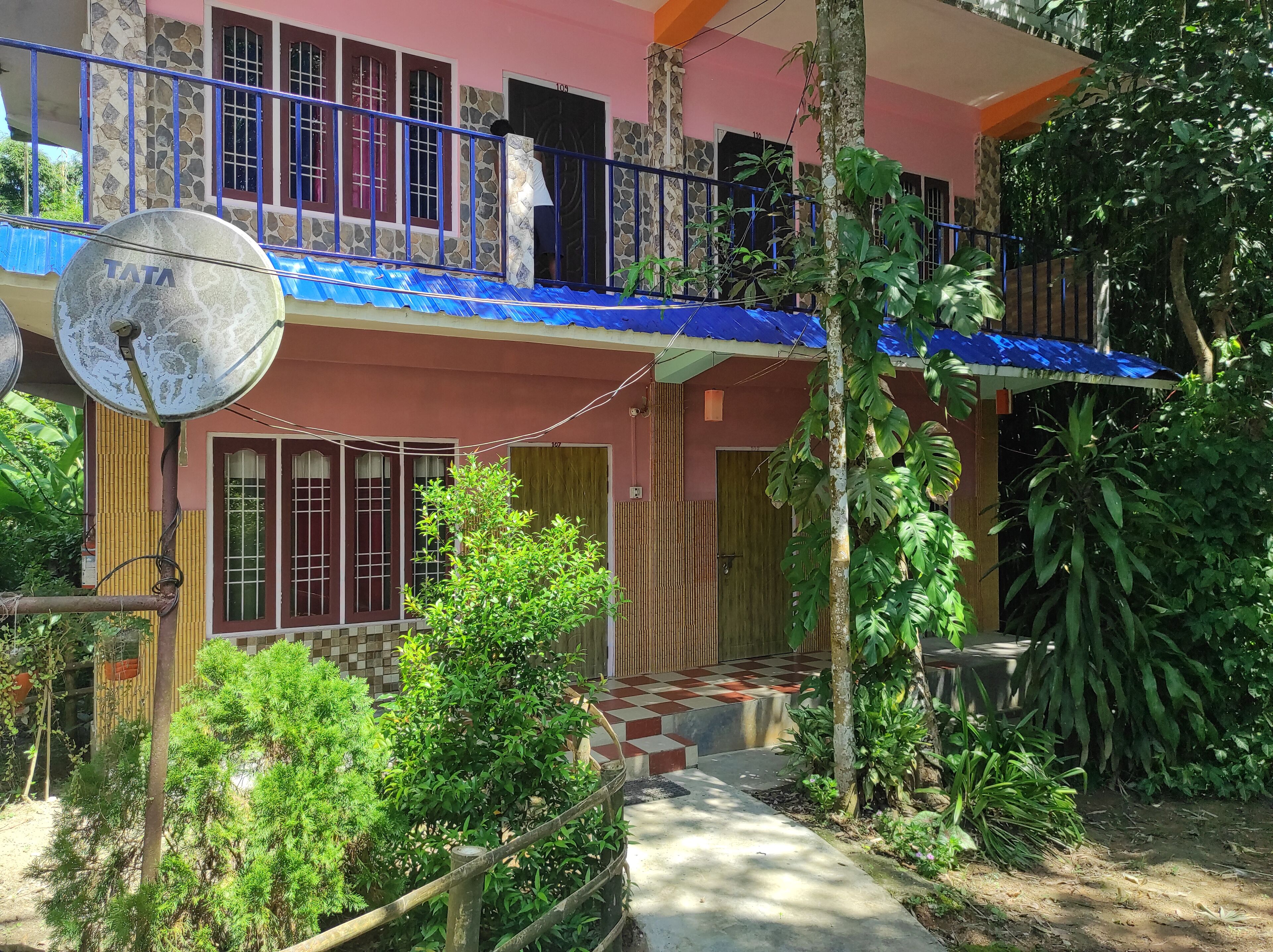 A two-story house with a satellite dish, a balcony, and a checkered pathway leading to the entrance.