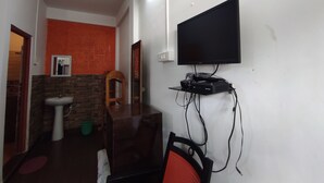 Une petite pièce, de taille modeste, avec un téléviseur fixé au mur, une table en bois, une chaise, un lavabo et un miroir.