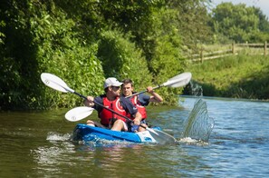 Zwei Personen paddeln mit ihren Kajaks auf einem von Grünflächen gesäumten Fluss.