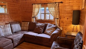 A cozy cabin interior with a brown leather sofa, plaid cushions, a small table, and a lamp. - Large Somerset lodge with access to adventure activities (East Huntspill)