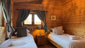 Una habitación de cabaña acogedora con dos camas, una mesita de noche y un ventanal con cortinas.