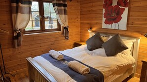 Une pièce de style cabane en bois, avec un lit, une fenêtre avec des rideaux et un grand tableau représentant des fleurs accroché au mur.