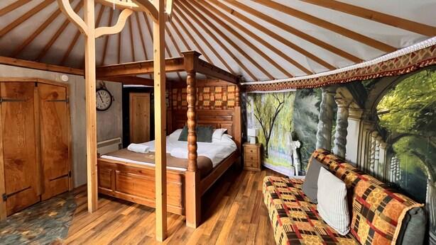 Een knus slaapkamer met houten inrichting, een hemelbed, een bank en een muurschildering van een boslandschap.