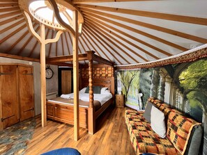 Une chambre chaleureuse, décorée dans un style rustique avec du bois, comprenant un lit à baldaquin, un canapé et une fresque représentant une scène de forêt.