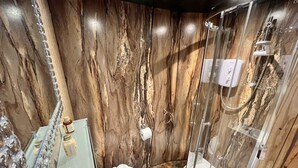 Een badkamer met een marmeren wand, een glazen douchecabine en een wit toilet.