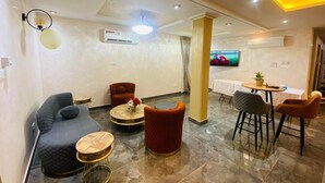 Un espace de détente moderne comprenant un canapé, des fauteuils, une table ronde et un téléviseur.