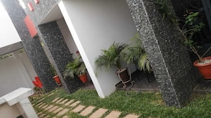 Une cour avec un chemin en pierre, des plantes en pot et un bâtiment blanc doté d’un portail noir.
