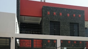 Un bâtiment à la façade rouge et noire, doté d’une entrée fermée par un portail et d’un patio aménagé avec une table et des chaises.