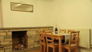 Un comedor con chimenea de piedra, sillas de madera, una mesa con mantel y una botella de vino.